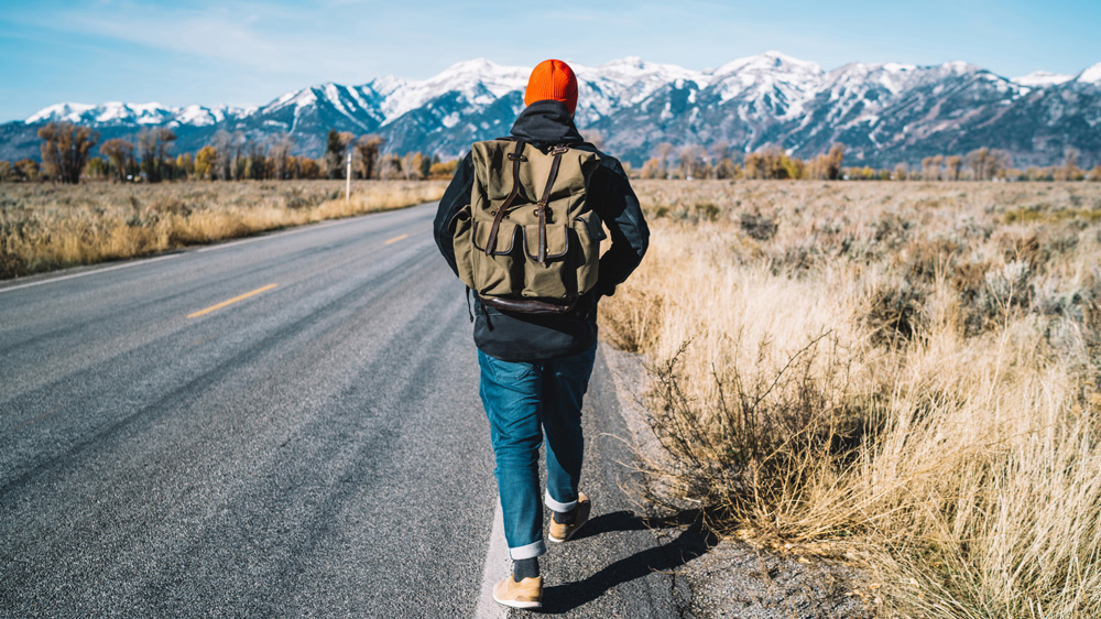 man walking down a highway through the countryside