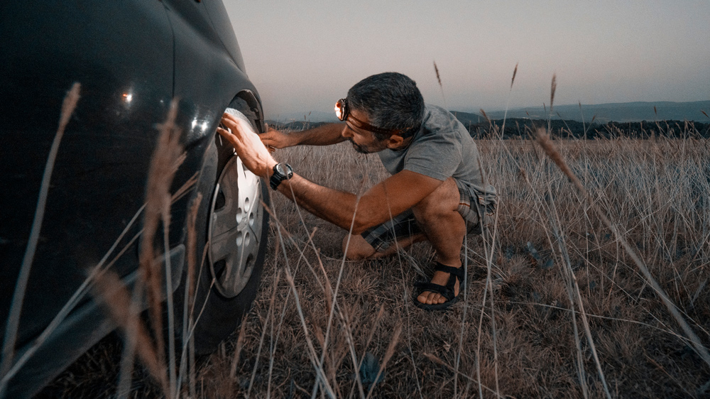 man examining a flat tire on his car in the countryside