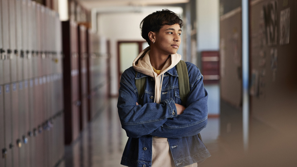 Teenage boy with arms crossed in hallway of lockers