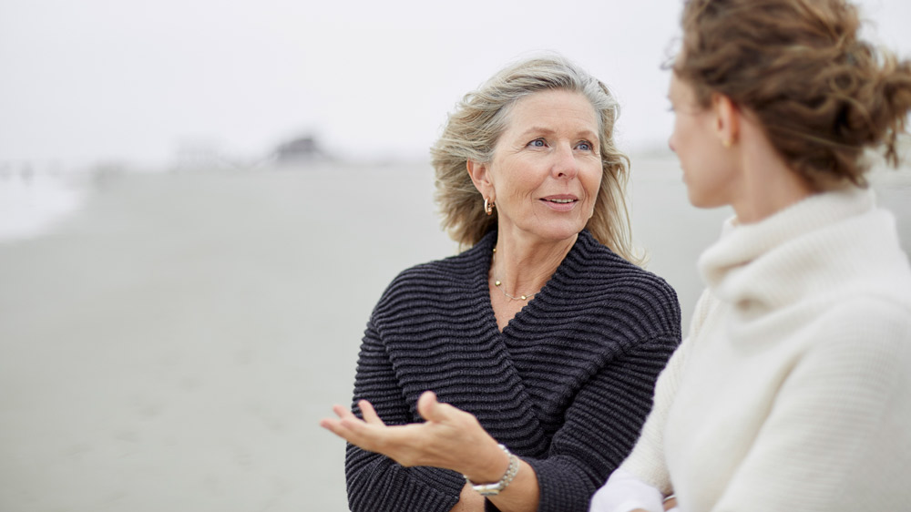 senior woman talking to adult daughter on the beach