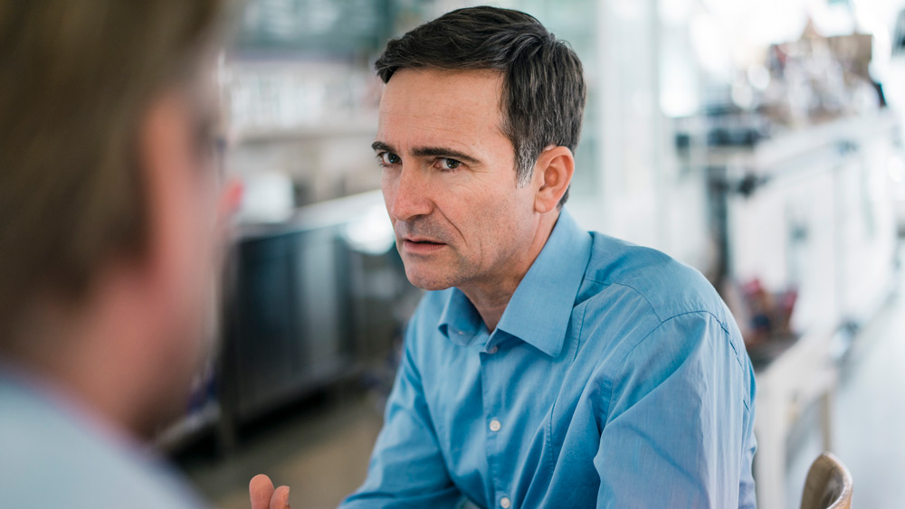 a man with concerned look on his face talking with another man in an office setting