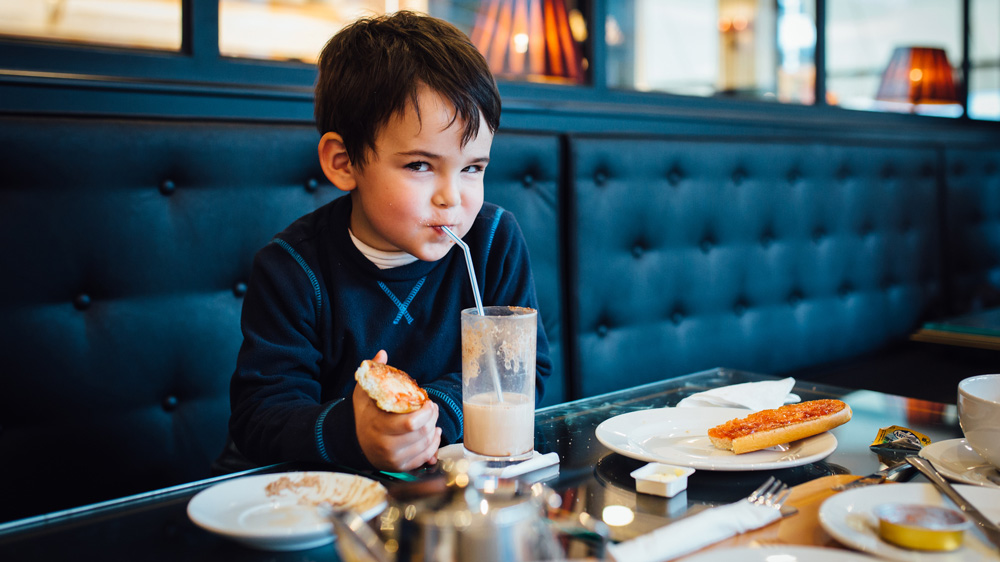 boy sitting in a cafe drinking a milkshake with devious look on his face