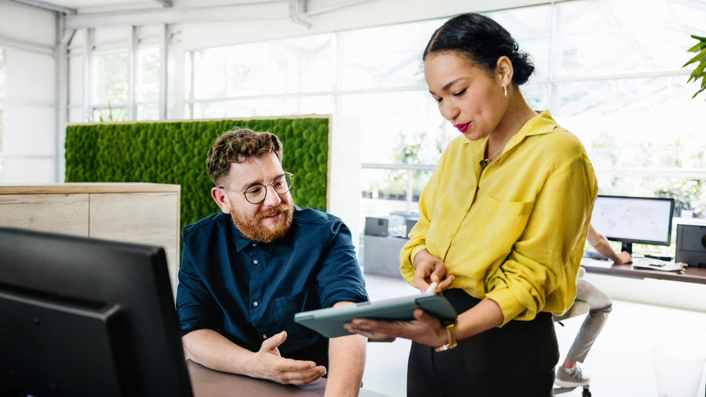 Office Manager Showing Documents On Digital Tablet To Colleague