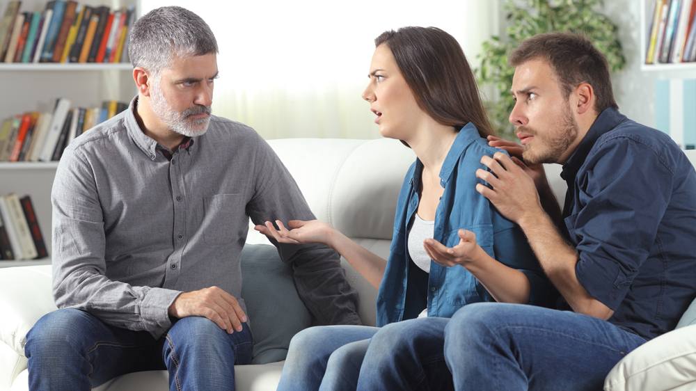 young couple talking with older gentleman on couch in home