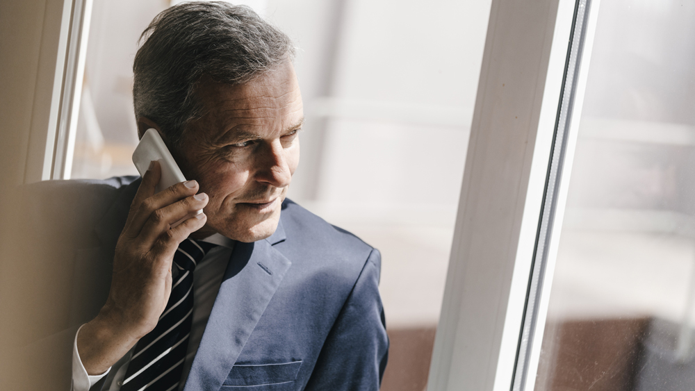 Smiling mature businessman on cell phone looking out of window