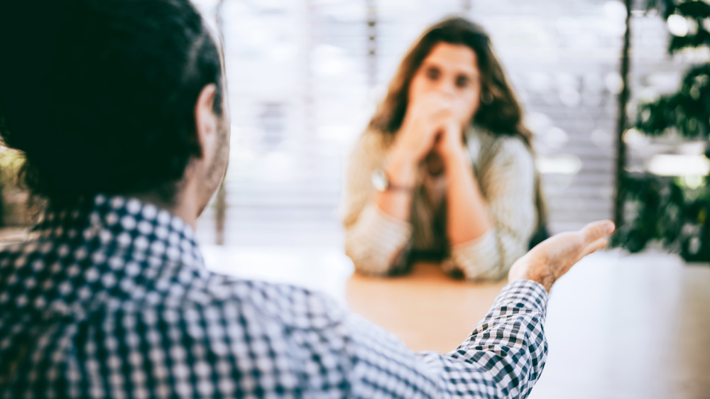 woman with arms defensively crossed talking with man at work