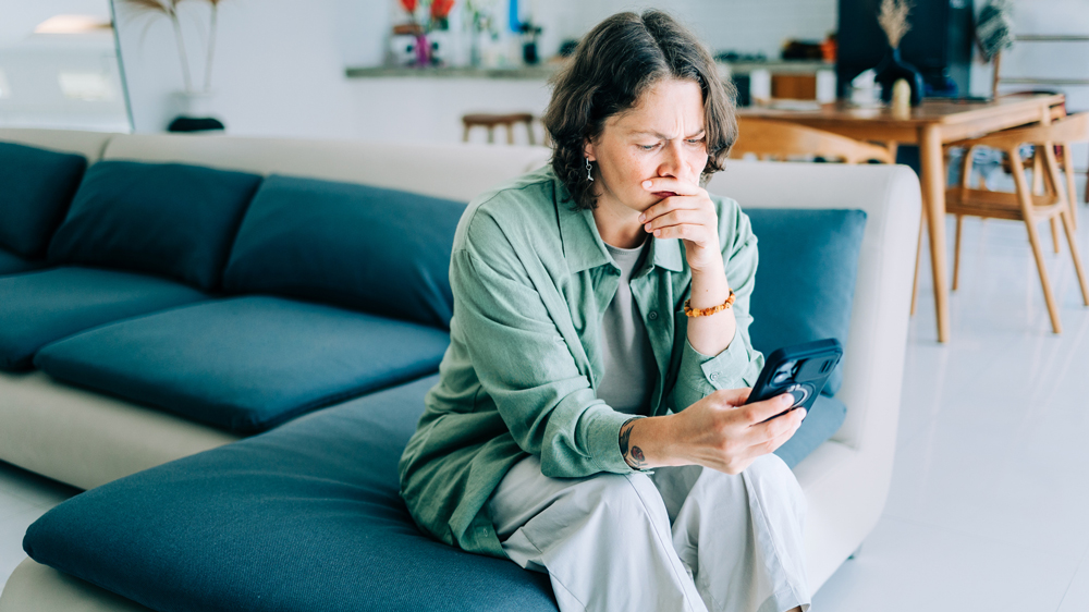 concerned woman sitting on couch looking at smartphone