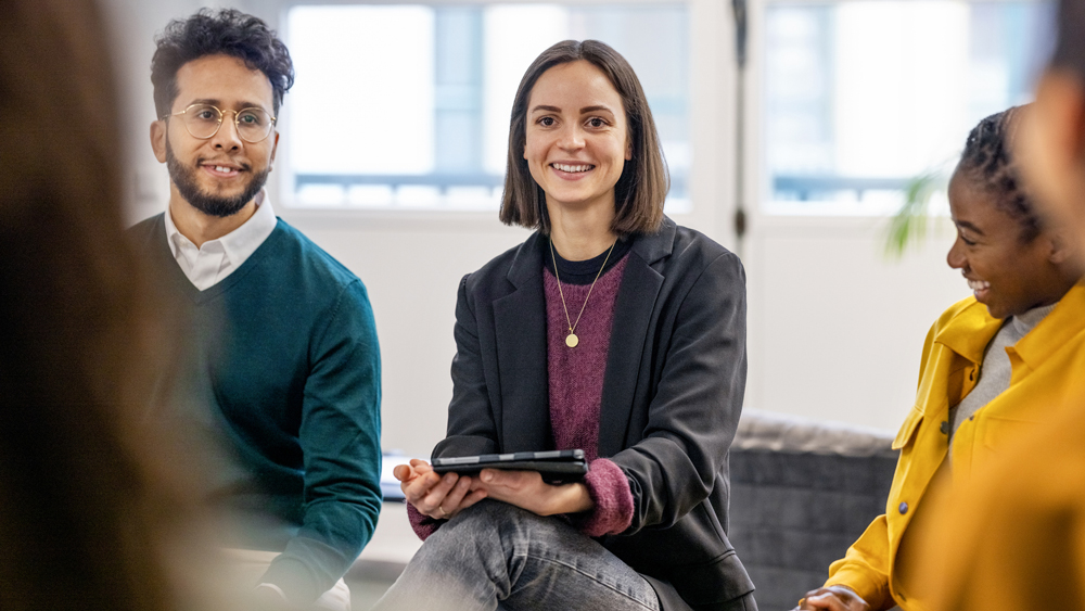Young woman holding digital tablet discussing work with team in office